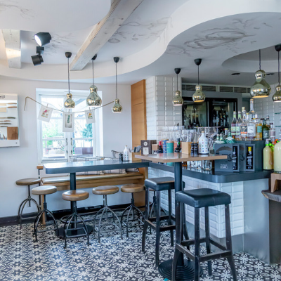Ein modernes Café-Interieur mit Barhockern, einer Theke, Hängelampen und dekorativem Bodenbelag.