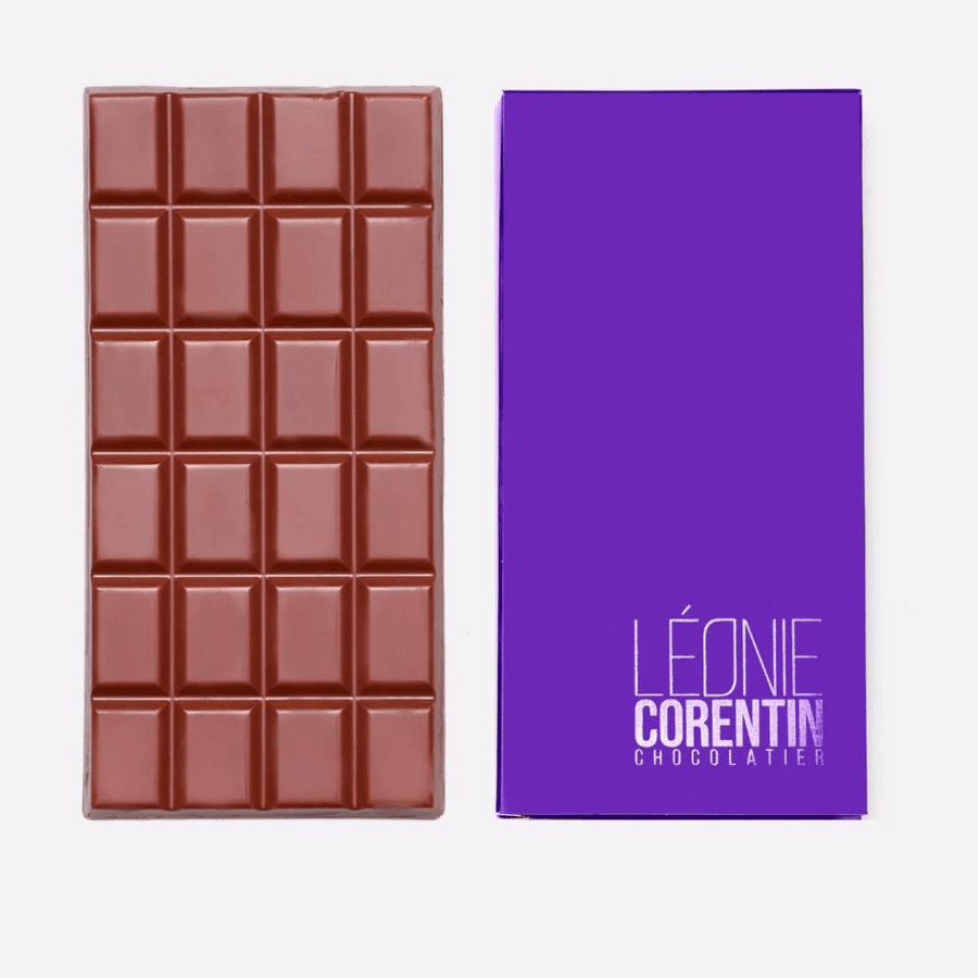 Eine **Léonie Corentin Vollmilchschokolade 45%** mit Gitterdesign steht neben ihrer violetten Verpackung, auf der in weißer Schrift „**Léonie Corentin**“ steht. Diese exquisite **Vollmilchschokolade** mit einem Kakaoanteil von 45% präsentiert die reichen Aromen von Kakao aus Bolivien.