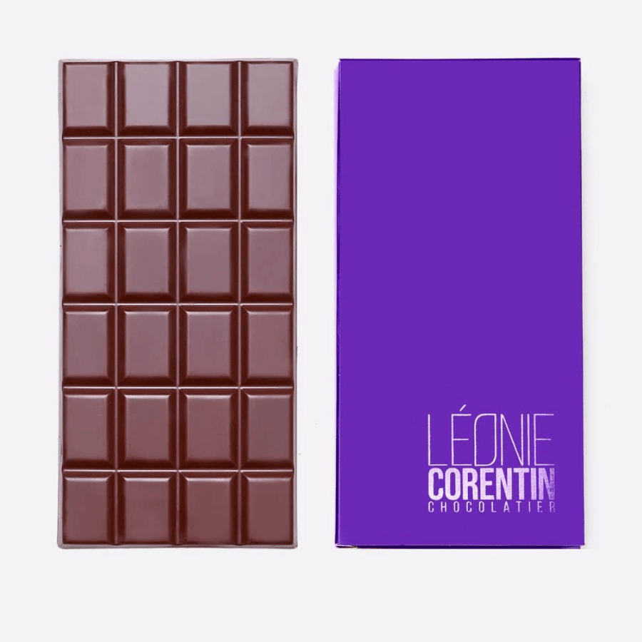 Neben einer violetten Verpackung mit der Aufschrift „Léonie Corentin“ wird eine Tafel Schokolade präsentiert. Die Léonie Corentin Zartbitterschokolade 72% ist in kleine quadratische Stücke unterteilt.