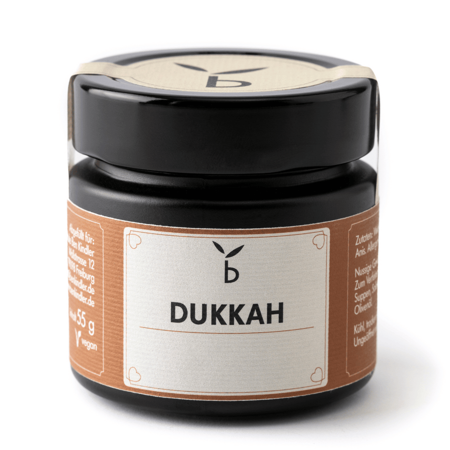 Vor einem weißen Hintergrund ist ein versiegeltes Glas mit der Aufschrift „benkindler. Dukkah“ zu sehen, das 55 Gramm der Gewürzmischung enthält. Das Glas hat einen schwarzen Deckel und ein braunes Etikett mit weißem Text, auf dem Inhalt und Spezifikationen angegeben sind.