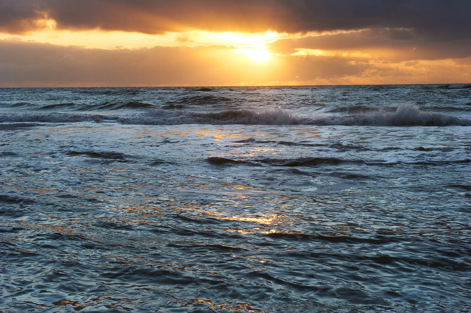 Ein Sonnenaufgang über einem aufgewühlten Meer mit Sonnenlicht, das durch die Wolken bricht und sich auf der Wasseroberfläche spiegelt.