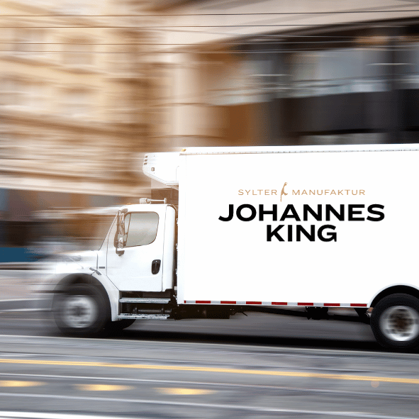 Ein weißer Lieferwagen mit der Aufschrift „Johannes King“ an der Seite wird in Bewegung auf einer verschwommenen Stadtstraße fotografiert.