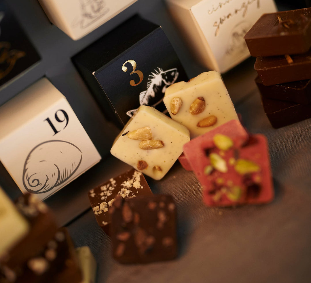 Eine Auswahl an Edelschokoladenstücken mit Nüssen und verschiedenen Toppings vor einem Johannes King Kings Schokoladen-Adventskalender 2023.
