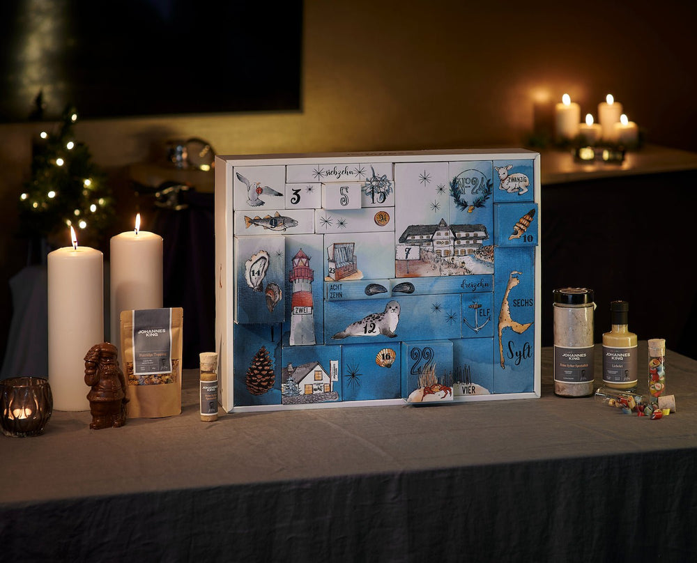 Ein dekorativer Sylter Manufaktur Feinkost-Adventskalender 2023 *für Familien* liegt auf einem mit Kerzen, Tannenzapfen und festlichen Gegenständen geschmückten Tisch und sorgt für eine warme und festliche Atmosphäre.