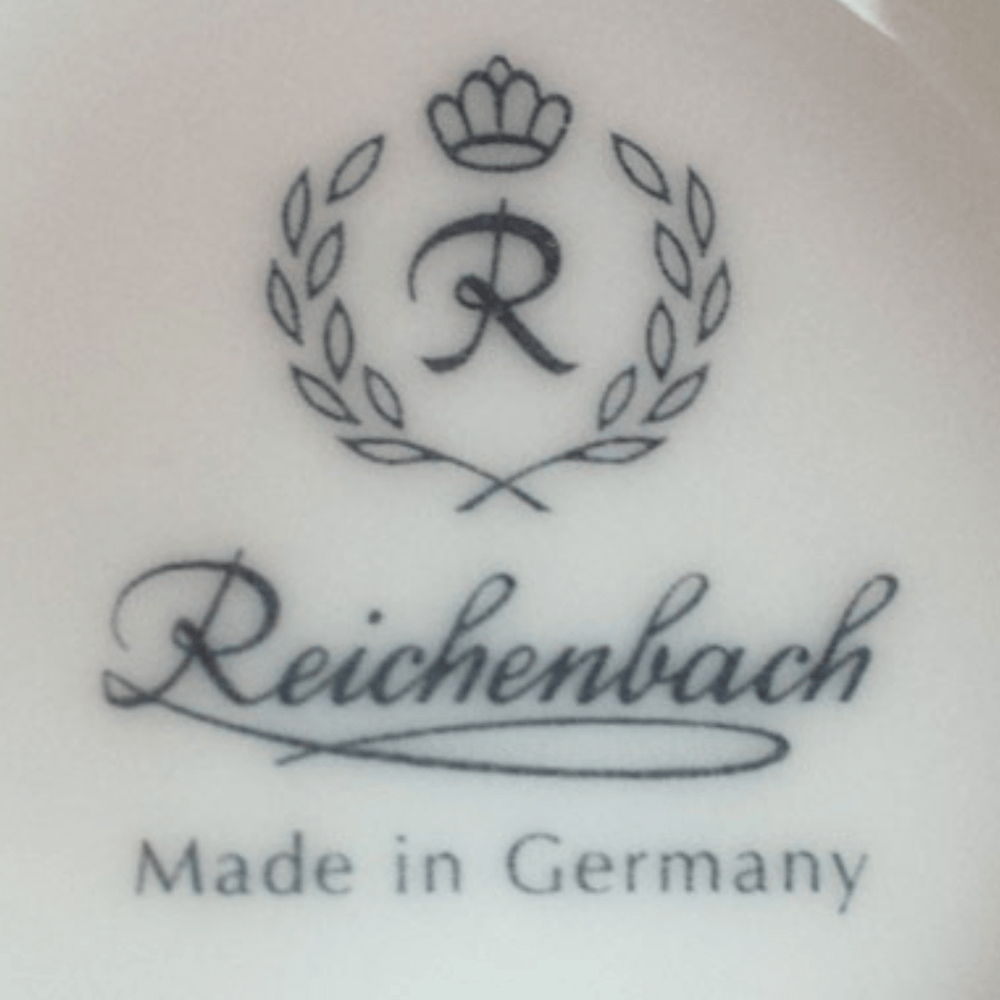 Eine Suppendose aus Porzellan mit dem Namen „Sylter Manufaktur“ unter einem stilisierten Buchstaben „r“, umgeben von einem Lorbeerkranzmotiv, mit dem Text „made in Germany“ darunter, alles auf der Oberfläche aufgedruckt.