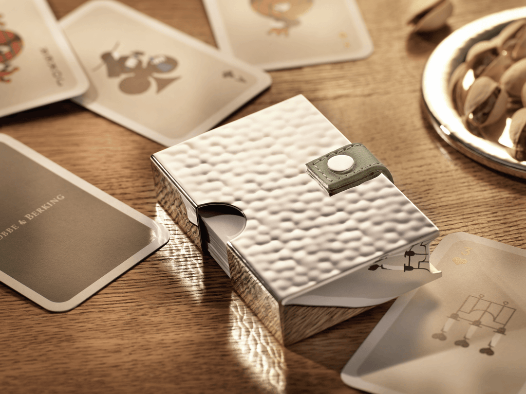 Luxuriöses Spielkarten Etui aus Silber mit Martelé Hammerschlag auf einem Holztisch, daneben Spielkarten und eine Silberschale mit Pistazien