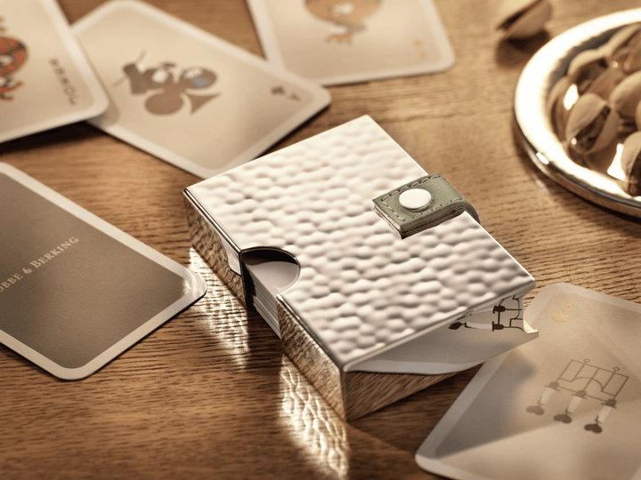 Luxuriöses Spielkarten Etui aus Silber mit Martelé Hammerschlag auf einem Holztisch, daneben Spielkarten und eine Silberschale mit Pistazien