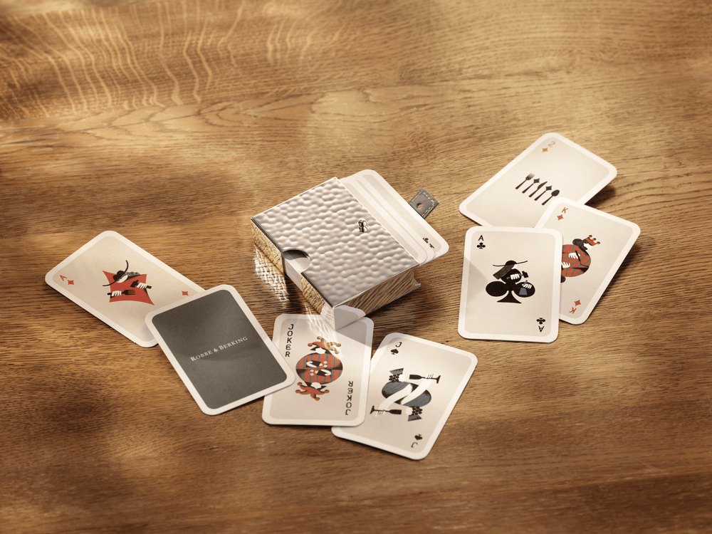 Spielkarten Etui aus Silber von Robbe & Berking auf einem Holztisch, umgeben von Spielkarten mit Joker, Kreuz Ass und Karo König