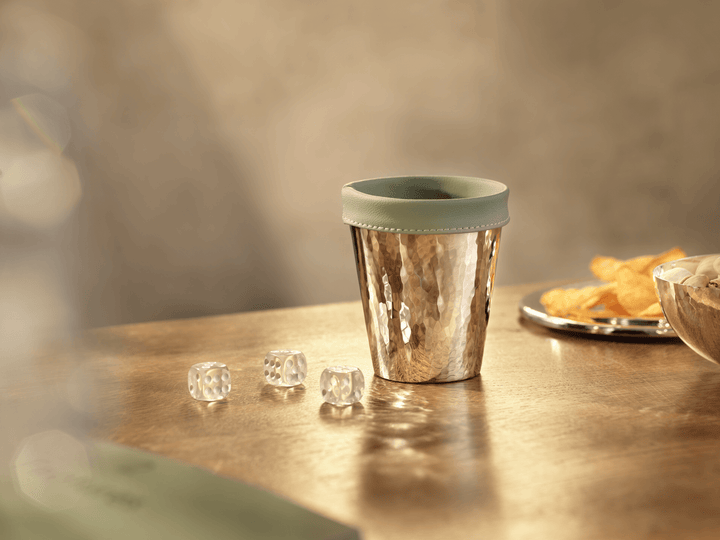 Handgehämmerter Würfelbecher aus Silber mit grünem Einsatz auf einem Holztisch, daneben drei Würfel und ein Silberteller mit Chips