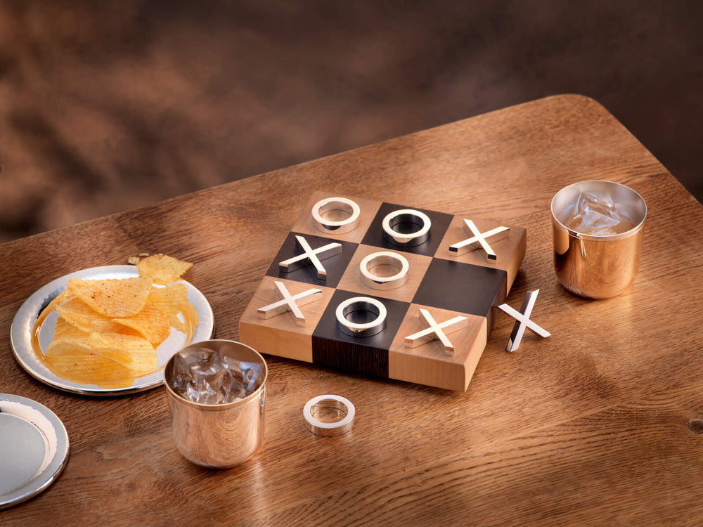 Luxuriöses Tic Tac Toe aus Silber und Holz auf einem Tisch, daneben versilberte Becher mit Eis und ein Teller mit Chips