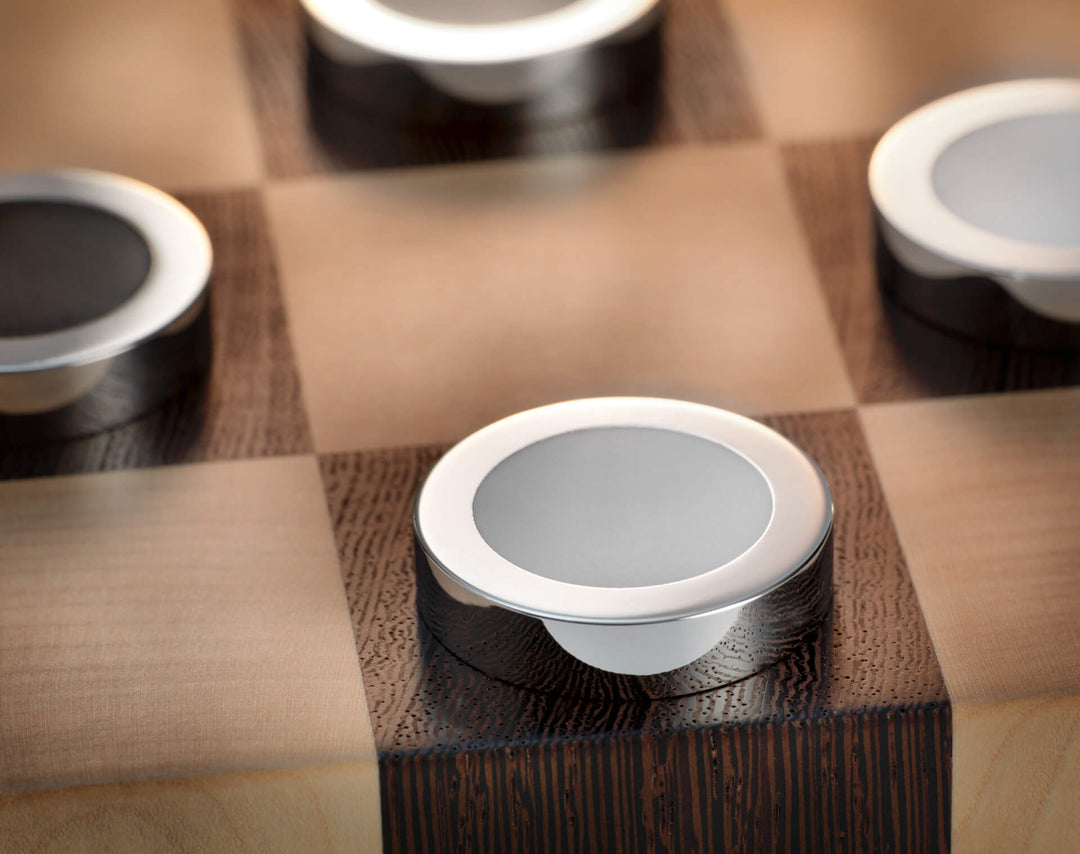 Versilberter Damestein mit heller Spielfläche auf einem dunklen Wengé Feld des Damebretts