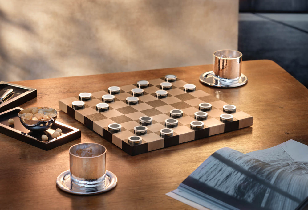 Luxuriöses Damespiel aus Silber von Robbe & Berking auf einem Holztisch, daneben Whiskybecher und Schale aus gehämmertem Silber