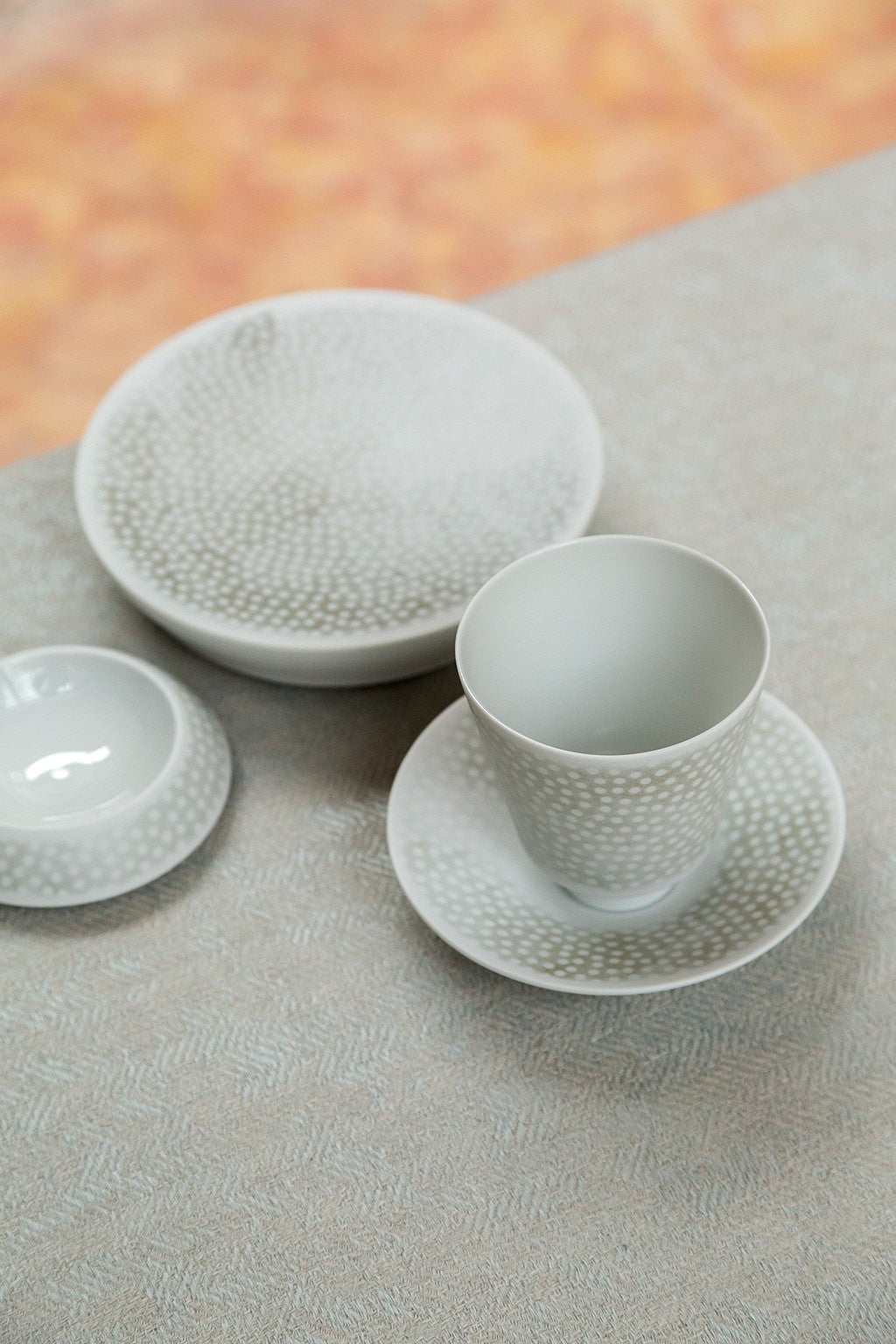 Ein Satz weißes, strukturiertes Keramikgeschirr auf einer hellen Oberfläche, darunter eine Tasse, eine Untertasse und zwei Teller.