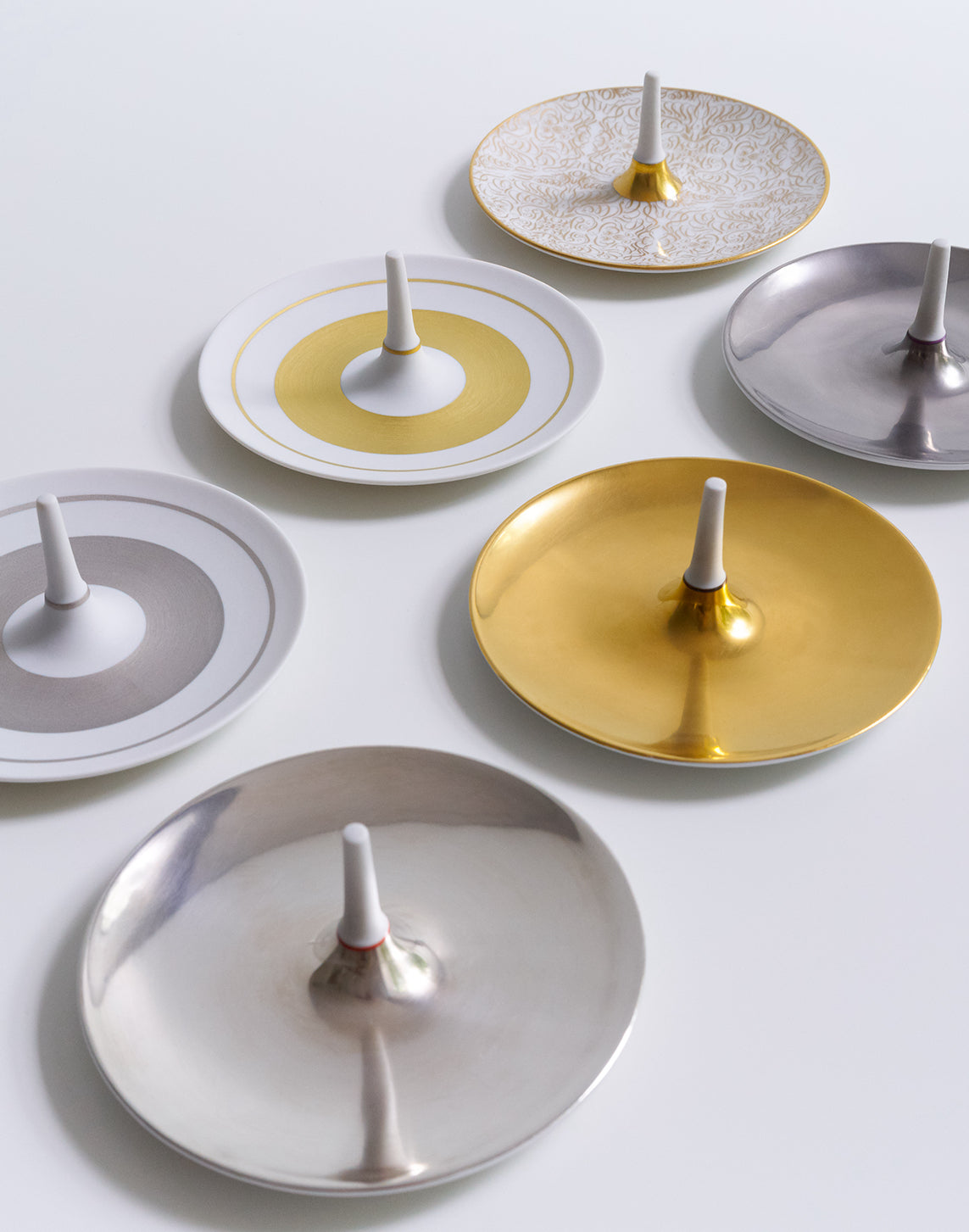 Eine Auswahl an dekorativen Tellern mit zentralen Vorsprüngen, die auf einer glatten Oberfläche angeordnet sind und verschiedene Designs und metallische Oberflächen aufweisen.