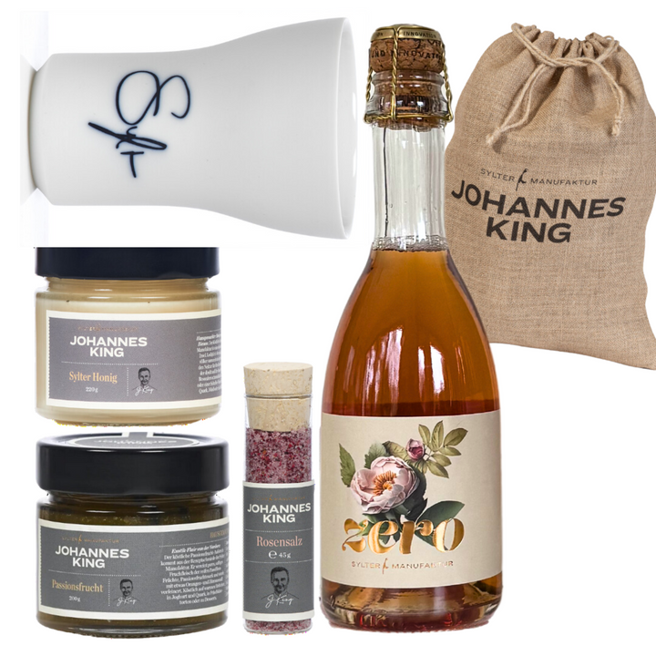 Das Nikolaus-Frühstück-Set der Sylter Manufaktur Johannes King umfasst eine Flasche mit Blumenetikett, zwei Gläser Honig und Brotaufstrich, ein kleines Döschen mit rosa Gewürzmischung und eine weiße Tasse mit blauer Signatur. Es wird in einem beigen Beutel mit Johannes King-Branding geliefert und ist somit das perfekte Nikolausgeschenk.