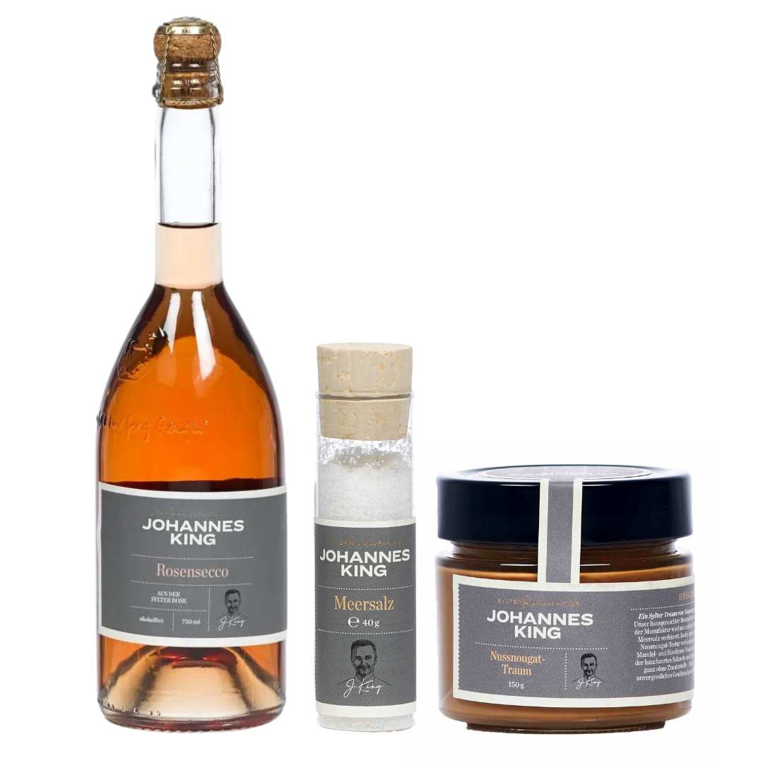 In einem edlen Display sind eine Flasche Johannes King Rosé Secco, eine Dose Sylter Meersalz und ein Glas Trüffelsenf zu sehen. Die Produkte der Marke Sylter Manufaktur Johannes King, bekannt als Sylter Spezialitäten für Gourmets, sind mit passenden Etiketten in edlem Grau und einer kleinen Portrait-Illustration versehen und eignen sich somit auch als Gourmet-Geschenk.