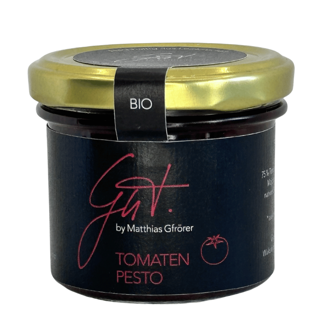 Ein Glas mit Tomatenpesto und der Aufschrift „Matthias Gfrörers Bio Tomaten-Pesto“ mit einem schwarzen Etikett mit rosa Handschrift und einem metallisch-goldenen Deckel mit der Aufschrift „Bio“.