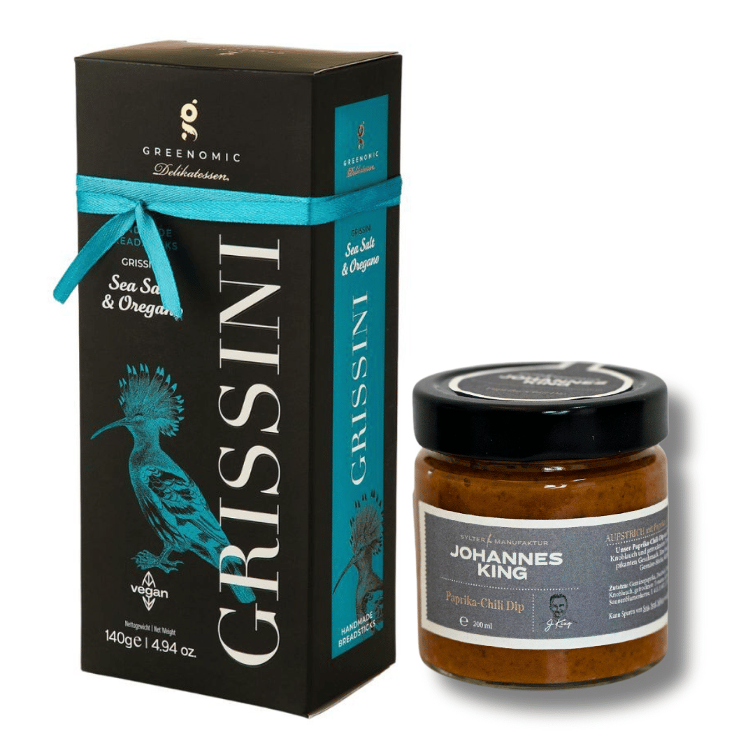 Das Bild zeigt eine Dose Paprika-Chili-Dip mit Grissini von der Sylter Manufaktur neben dem beiliegenden Dipglas. Die Grissini-Dose ist mit einer blauen Schleife zugebunden, das Dipglas hat einen schwarzen Deckel mit grauem Etikett.