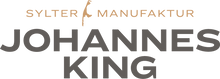Das Bild zeigt das Logo für „Johannes King Sylter Manufaktur“, das wie ein Markenname aussieht, mit stilisiertem Text und einem grafischen Element, das an einen tropfenden Löffel oder eine Inselsilhouette über dem Buchstaben „i“ in „Sylter“ erinnert.