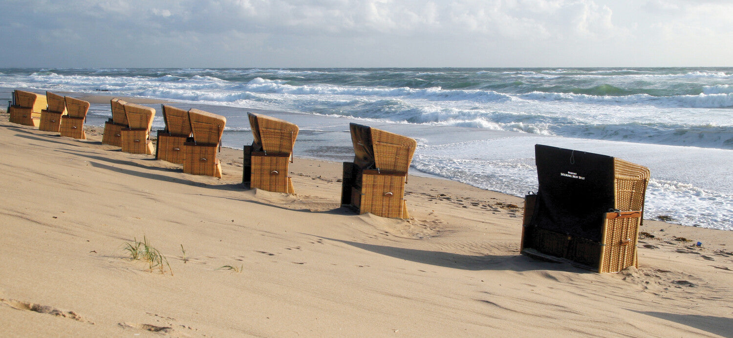 Eine Reihe von Strandkörben mit Blick auf das Meer an einem Sandstrand, im Hintergrund brechen die Wellen.