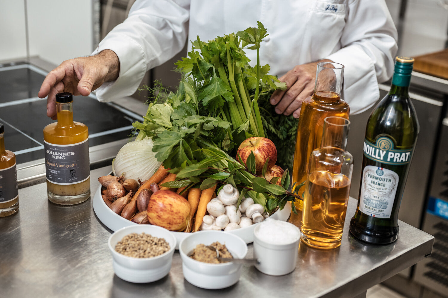 Ein Koch bereitet auf einer Küchentheke aus Edelstahl Zutaten zum Kochen vor, darunter frisches Gemüse, Gewürze und Würzmittel.