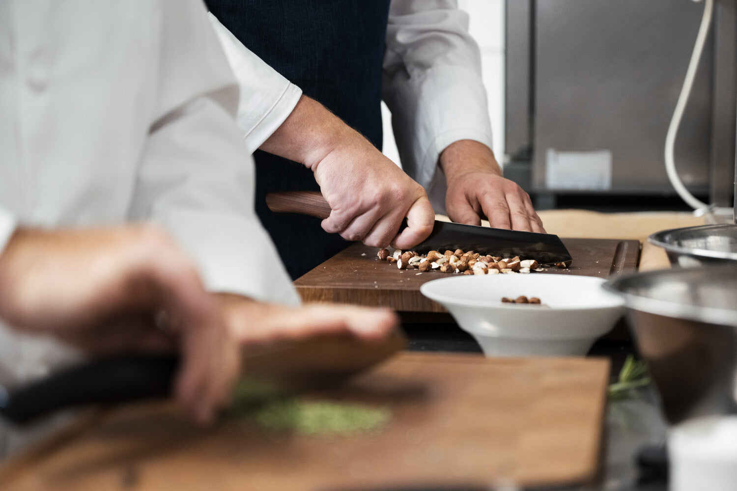 Ein Koch hackt in einer professionellen Küche sorgfältig Nüsse auf einem Holzschneidebrett.