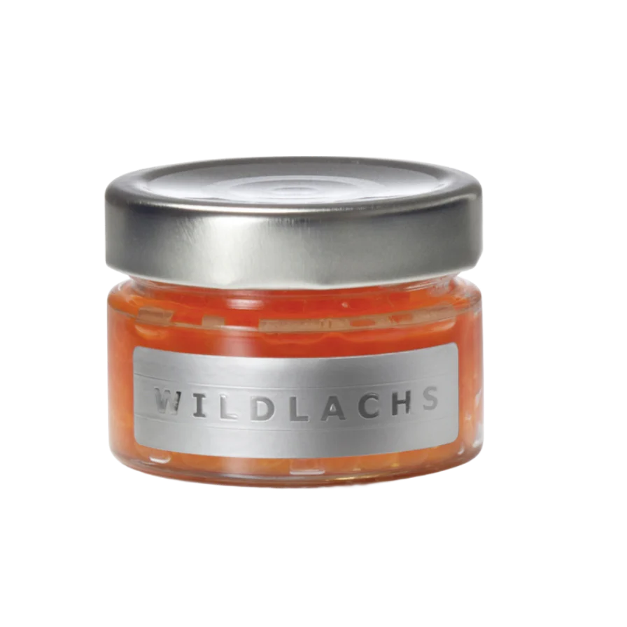 Ein kleines Glasgefäß mit einem silbernen Metalldeckel, das orangefarbene Fischstücke enthält, beschriftet mit "Wildlachs Kaviar" von Dieckmann & Hansen.