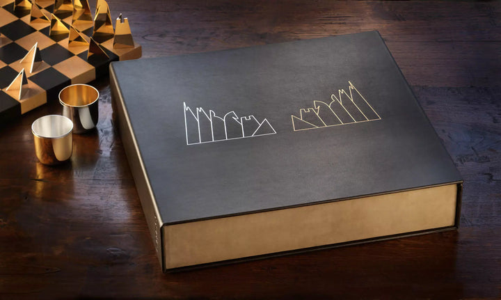 Geschlossene Aufbewahrungsbox aus dunklem Leder mit Figuren Silhouetten in Silber und Gold, daneben zwei Becher