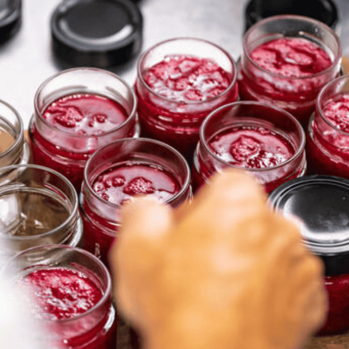 Gläser mit frisch zubereiteter Kings Rosa Rugosa Rosenaufstrich-Marmelade in verschiedenen Stadien der Abfüllung und Versiegelung auf einer Küchenoberfläche der Sylter Manufaktur.