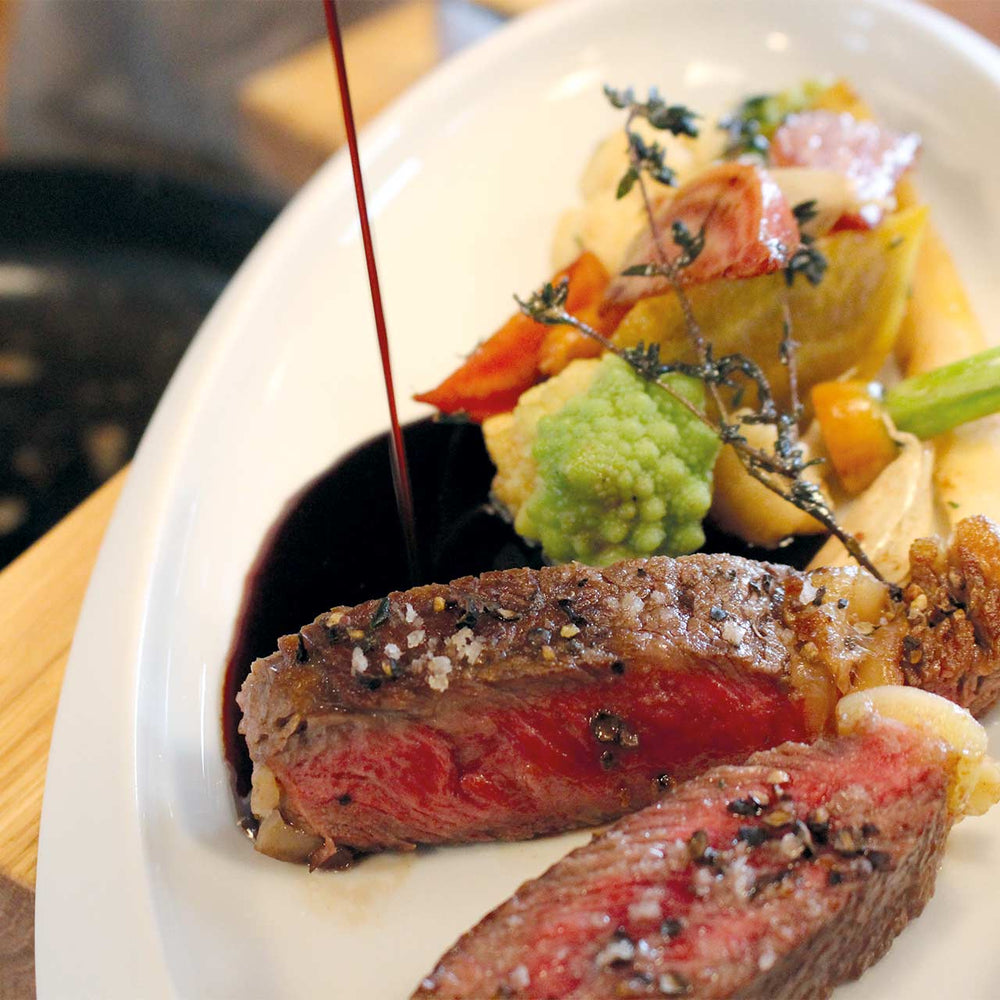 Ein Strahl dunkler Sylter Manufaktur Kings Saucen-Doping wird auf einen Teller gegossen, der aus einem in Scheiben geschnittenen medium-rare Steak, dazu Gemüse und Kartoffeln besteht.