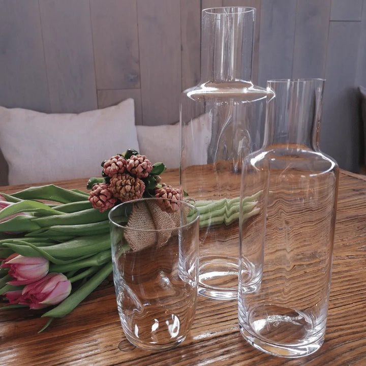 Verschiedene Jolie Glas Quetschglas eingedrückte Glaskaraffen 0,5 l auf einem Holztisch neben einem in Sackleinen gewickelten Strauß rosa Tulpen angeordnet.