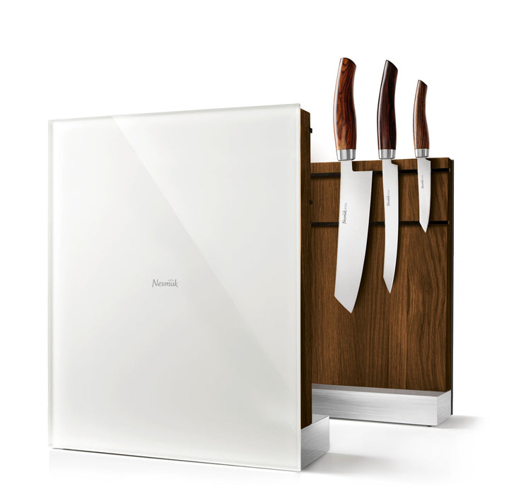 Ein Set aus drei Küchenmessern mit Holzgriffen, eingesetzt in einem hölzernen Messerblock, ausgestellt neben einem weißen Nesmuk-Messerhalter, ausgestattet mit Hochleistungsmagneten.