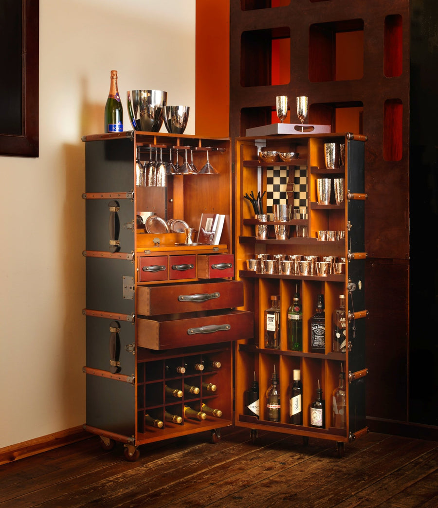 Ein gut organisierter Robbe & Berking Barschrank im Kofferdesign schwarz – mit Ausstattung, der eine Auswahl an alkoholischen Getränken, Gläsern und Barzubehör enthält, neben einer Wand.