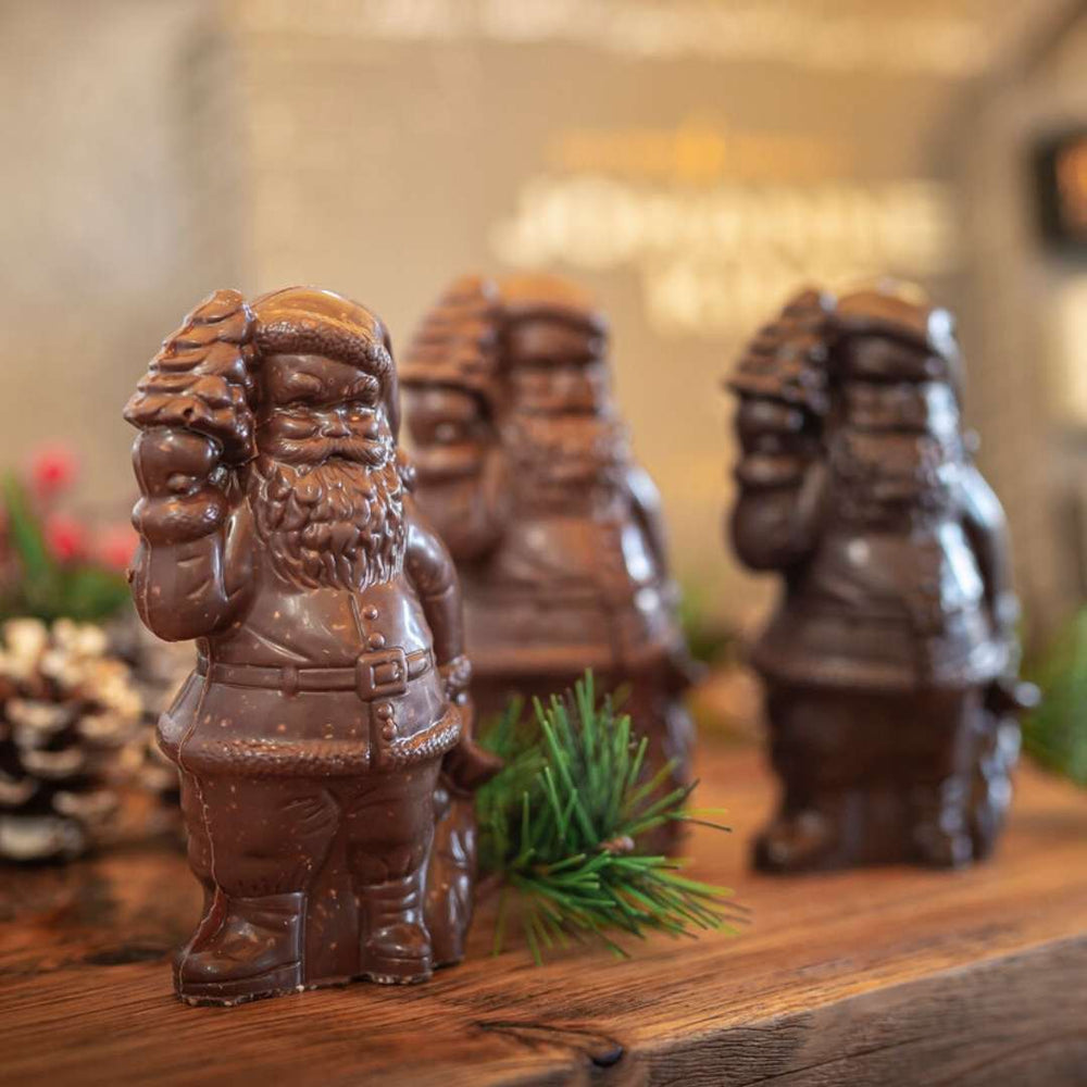 Kings Schokoladen-Weihnachtsmann Salzkaramell-Figuren der Sylter Manufaktur aufgereiht auf einer Holzunterlage mit einem Tannenzweig im Vordergrund.