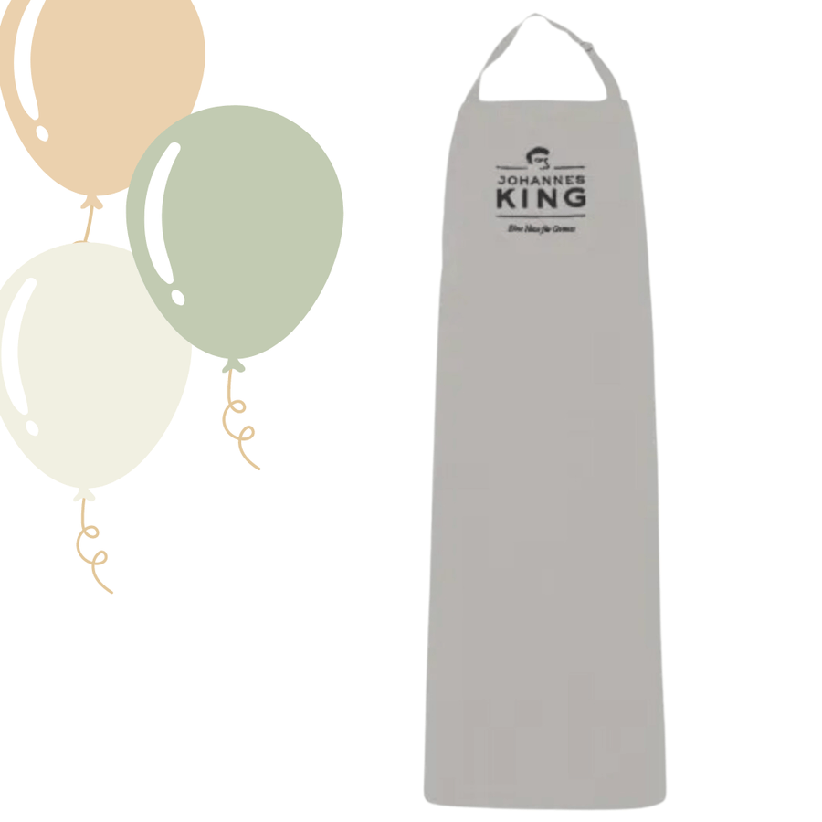 Eine „Kings Kochschürze Mischgewebe grau“ der Marke „Sylter Manufaktur“ mit dem Logo von „Johannes King“, einem renommierten Sternekoch, überlagert auf einem neutralen Hintergrund, begleitet von einfachen Illustrationen von drei Luftballons auf der linken Seite.