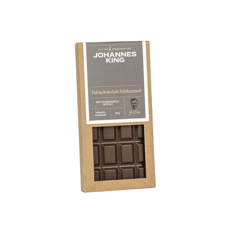 Eine Tafel Schokolade mit der Aufschrift „Sylter Manufaktur“ und einer teilweise ausgepackten Tafel dunkler Schokolade von Kings Salzkaramell Tafelschokolade, unter der ordentliche Reihen von Schokoladenquadraten sichtbar sind.