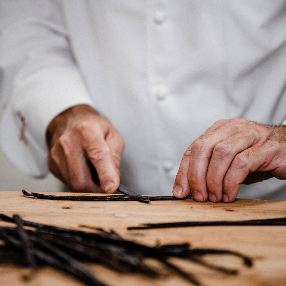 Ein Koch bereitet vorsichtig Vanilleschoten auf einer Holzoberfläche vor, vermutlich für die Verwendung in einem Dessert der Marke Sylter Manufaktur Kings „Liebeleigroß“.