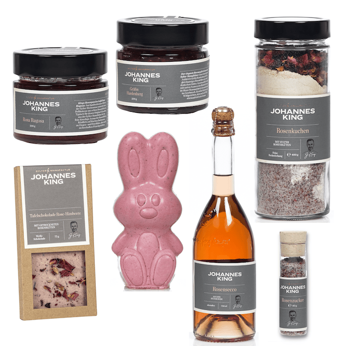 Eine Auswahl an Gourmet-Lebensmitteln, darunter Schokoladenaufstriche, ein Rosiger Ostergruß, eine Flasche Rosensekt und eine Dose Rosenzucker, alle mit der Marke „Sylter Manufaktur Johannes King“.