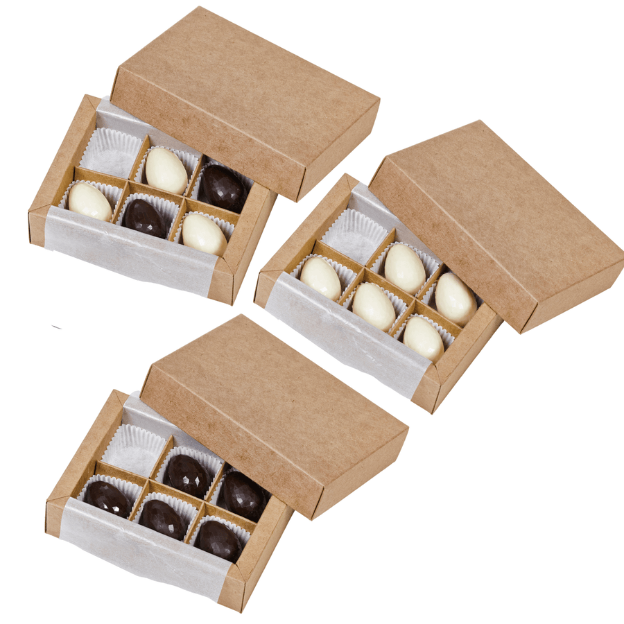 Drei Schachteln Sylter Ostereier-Parade-Pralinen, darunter sowohl dunkle als auch weiße Schokoladensorten, teilweise geöffnet, um ihren Inhalt zu präsentieren. Diese handgegossene Schokoladenauswahl ist das perfekte Ostergeschenk der Sylter Manufaktur.