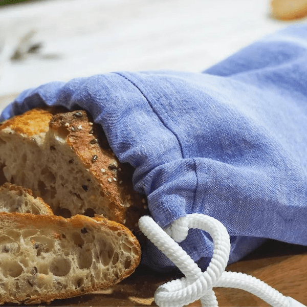 Eine Scheibe frisch geschnittenes Brot, teilweise in einem Dorothea Waydsch Große Brotzeit – Set aus Leinen eingewickelt, mit Kordelzug auf einer Holzoberfläche.