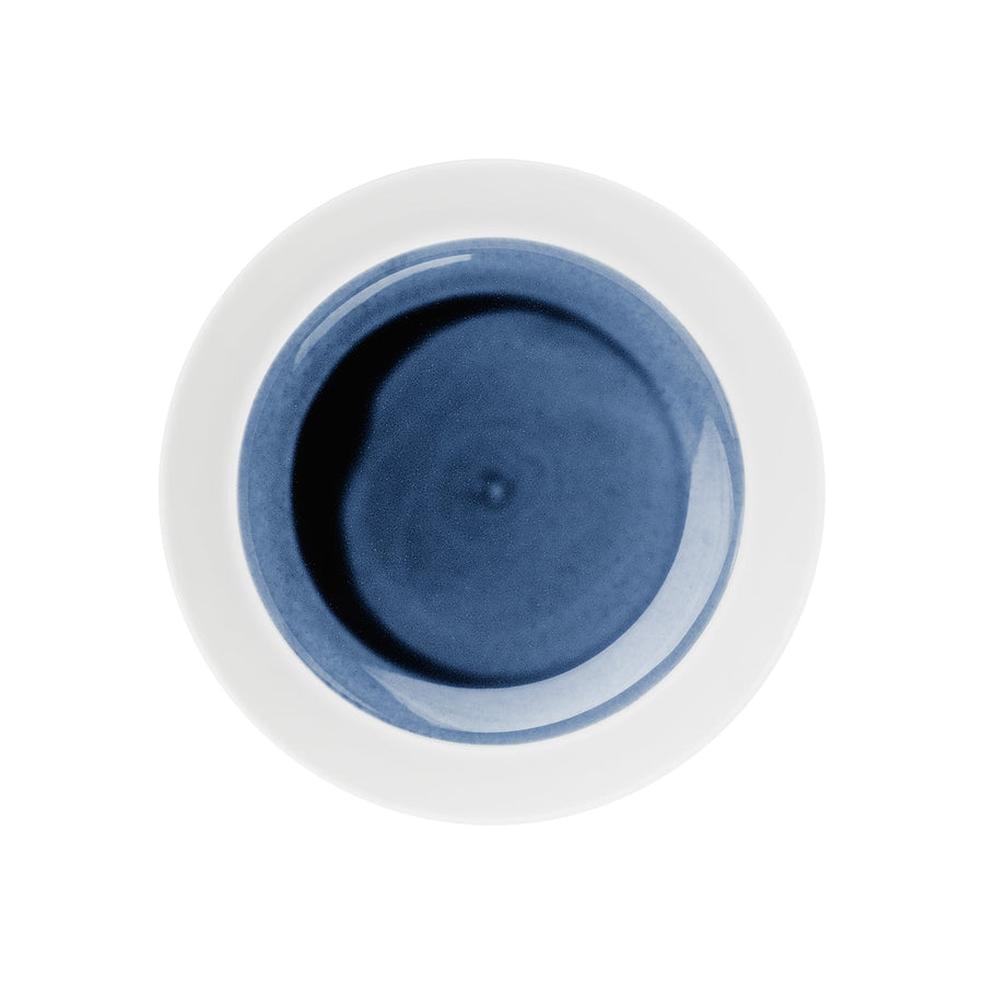 Satz mit ersetztem Produkt- und Markennamen: Ein weißer runder Hering Berlin flacher Teller, hoher Rand Blue Silent Teller mit einer dunkelblauen Flüssigkeit, zentriert auf einem weißen Hintergrund.