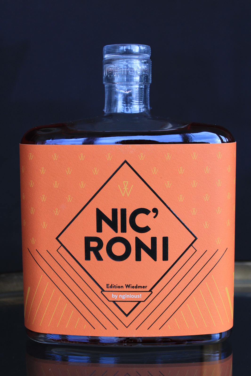 Eine Flasche mit einem leuchtend orangefarbenen Etikett mit der Aufschrift „Nicroni edition wiedmer by ninoust“ vor dunklem Hintergrund.