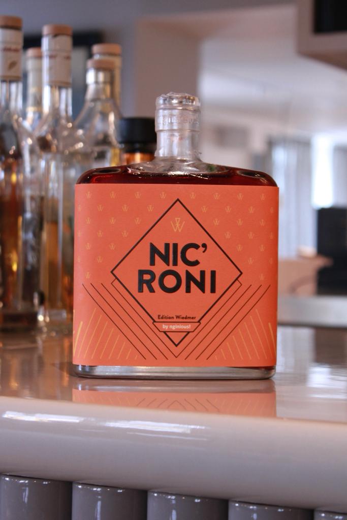 Eine Flasche italienischer Whiskey Nicroni von Nevrland steht auf einer Bar, im Hintergrund sind verschiedene andere Flaschen zu sehen.