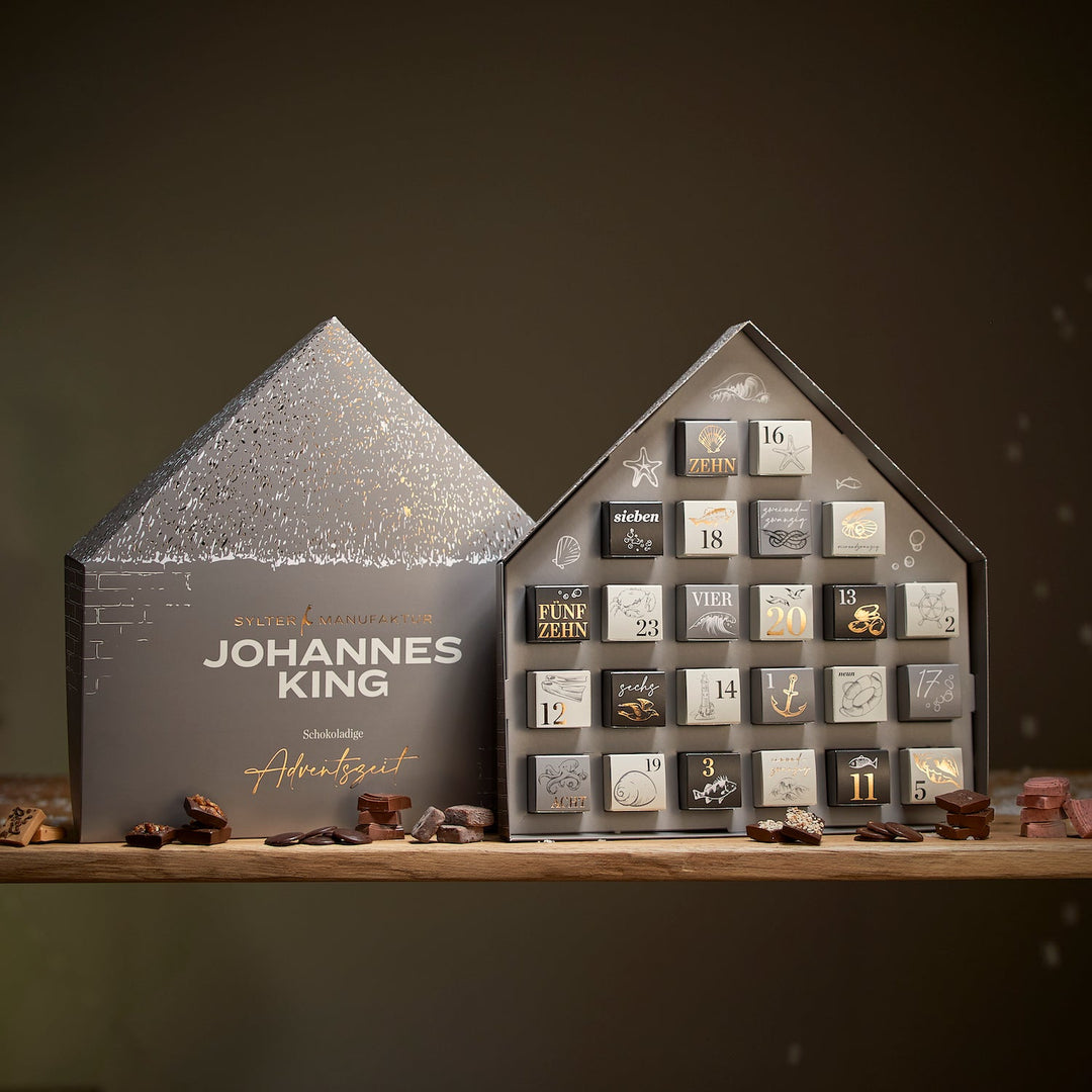 Ein 6er-Set Schokoladen-Adventskalender der Sylter Manufaktur Johannes King, gestaltet als zweidimensionale Häuser mit nummerierten Fächern, gefüllt mit verschiedenen Schokoladen, eine Tür lässt sich öffnen, um einen Leckerbissen preiszugeben.