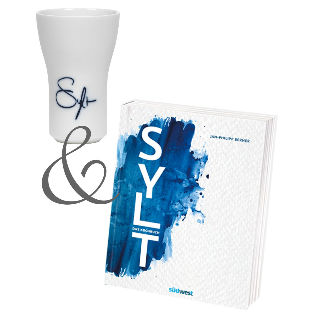 Ein weißer SYLT-Kochbuch & Hering Berlin Becher neben einem weißen Trinkglas mit blauer Sylter Manufaktur Johannes King-Aufschrift und einem Autogramm.
