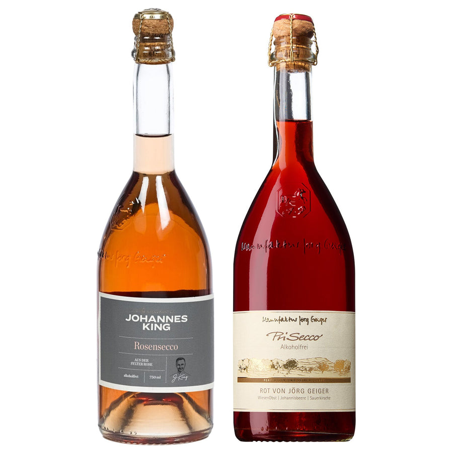 Zwei Flaschen Alkoholfrei anstoßen, eine mit klarer Flüssigkeit, die andere rot, beide mit der Aufschrift „Sylter Manufaktur Johannes King Prisecco“.