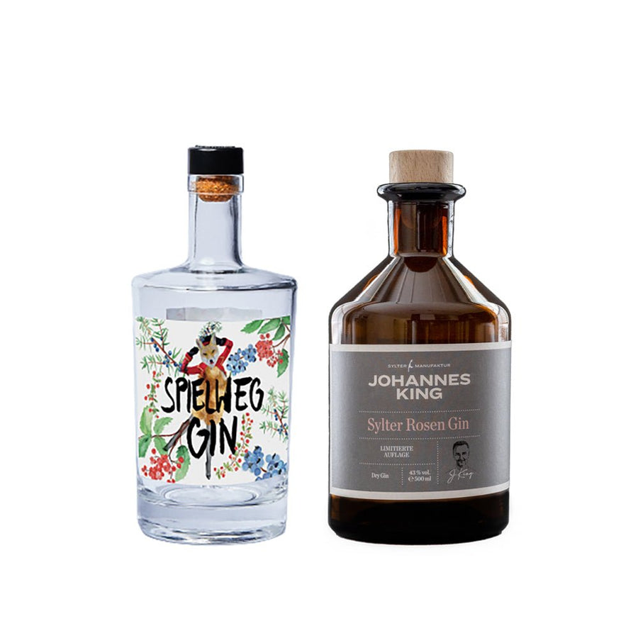 Zwei Flaschen 2x Gin macht Sinn mit markanten Etiketten, eine mit der Marke „Rosengin“ mit floralem Design und die andere „Schwarzwälder Spielweg Gin“ mit dunklem Etikett und Holzverschluss, präsentiert vor einem
