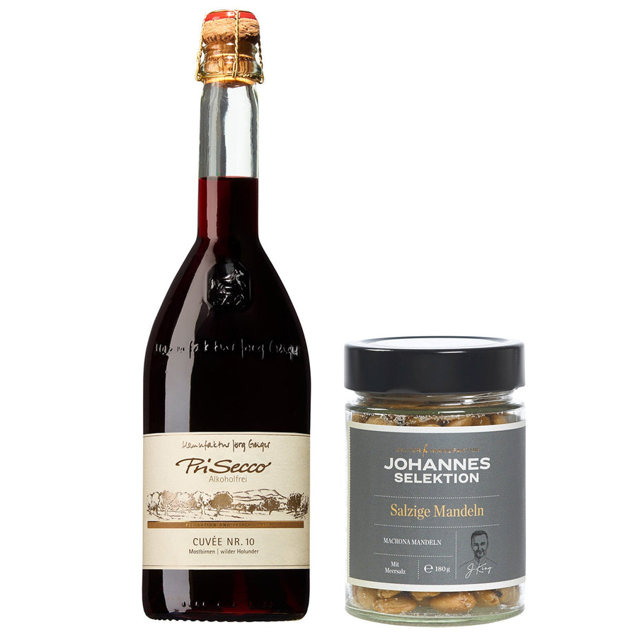 Eine Flasche alkoholfreier Begrüßungs-Prosecco und ein Glas salzige Mandeln auf weißem Hintergrund. Markenname: Sylter Manufaktur Johannes King