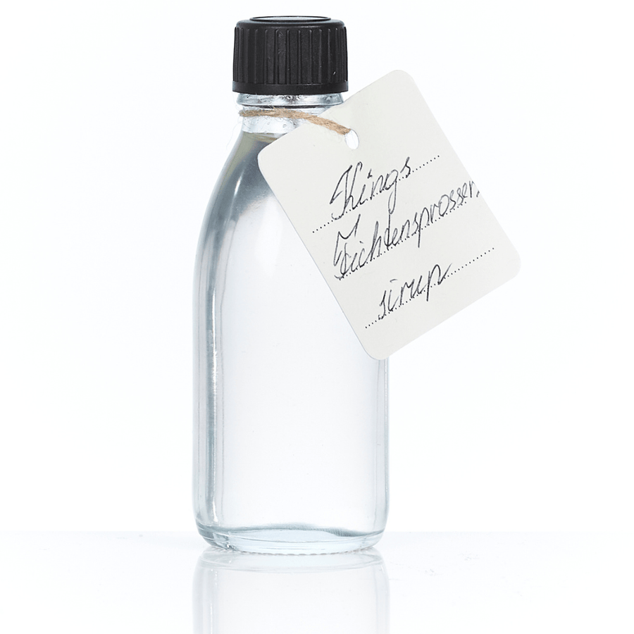 Klare Glasflasche mit handgeschriebenem Sylter Manufaktur Fichtensprossen-Sirup-Etikett mit Bindfaden und schwarzem Verschluss.