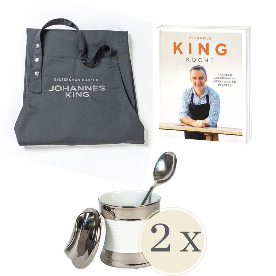 Eine Werbeaktion *Sylter Manufaktur Johannes King* mit einer Einkaufstasche mit dem Aufdruck „Sylter Manufaktur Johannes King“ und einem Kochbuch von Johannes King mit dem Titel „Kocht“ mit seinem Bild darauf
